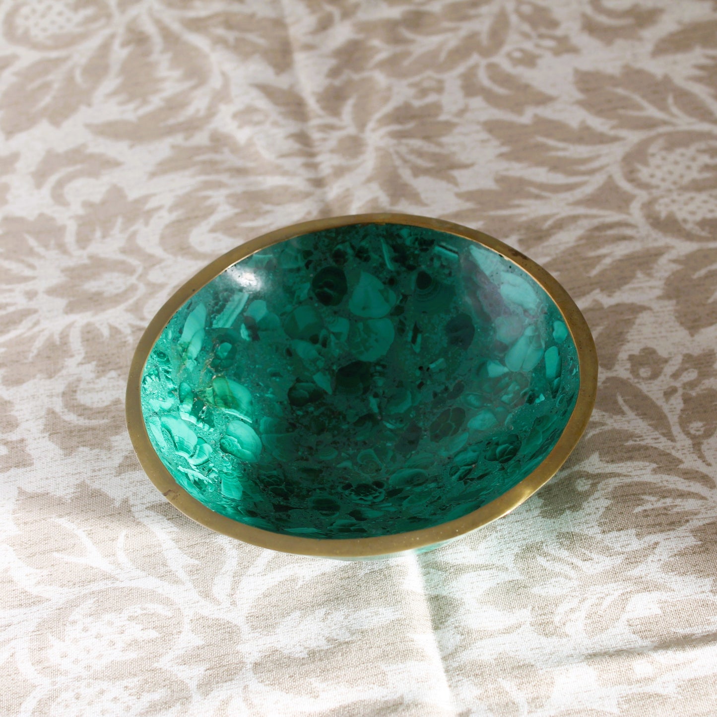 Green marbled bowl with gold rim on a textured beige surface