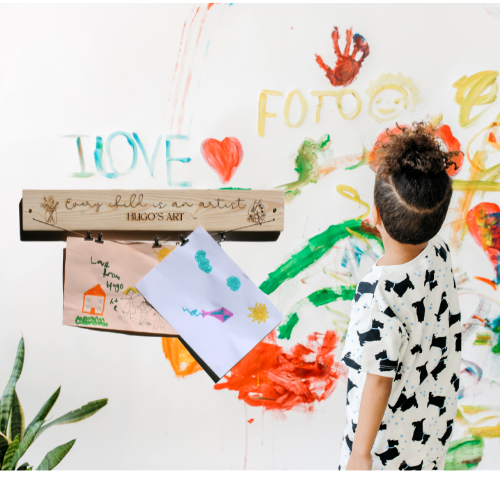 Child standing in front of a wall with colorful art and a wooden sign.