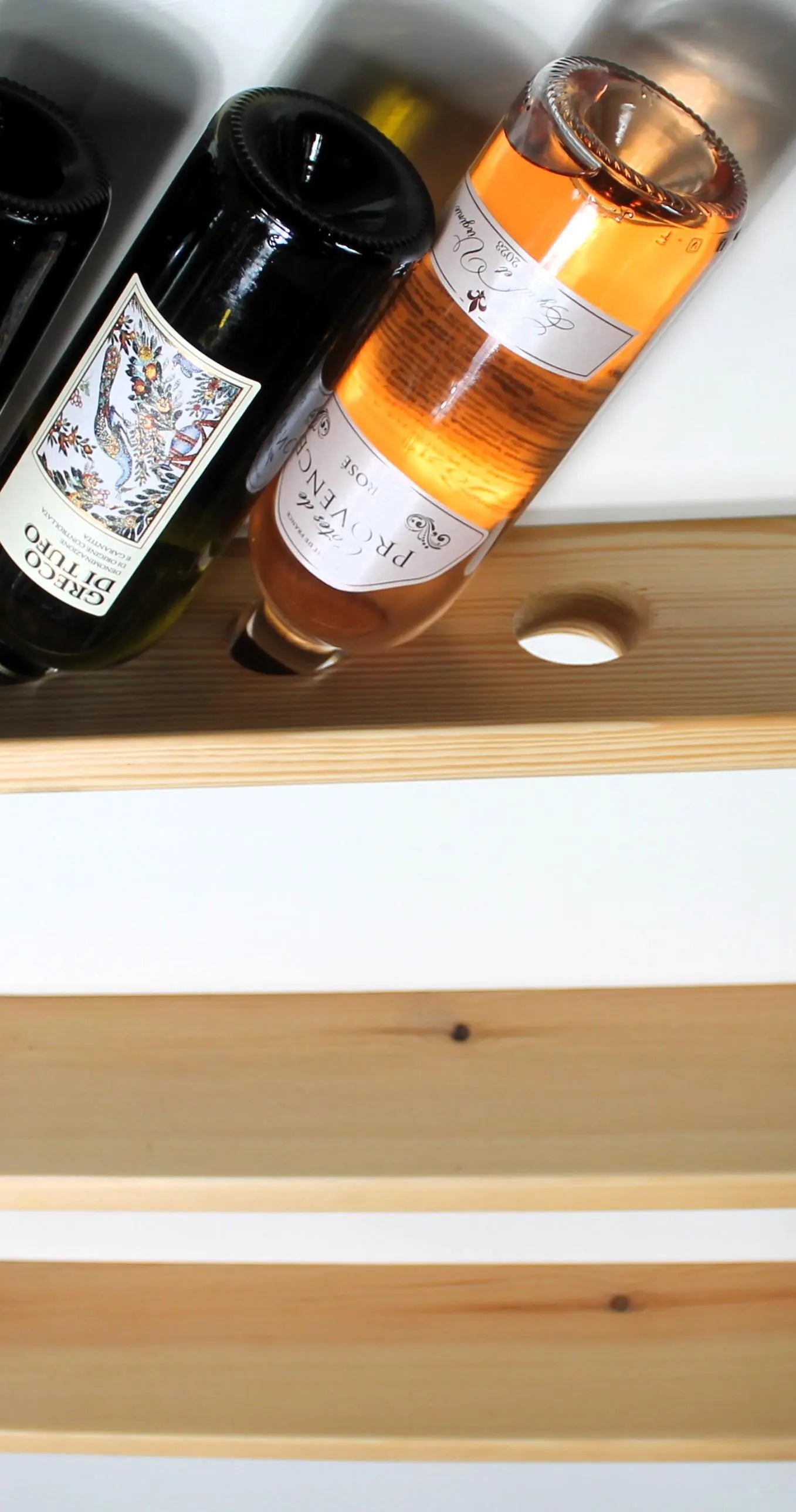 Three light natural wood floating shelves with oval cutouts, shown against a white wall with wine bottles partially resting on the top shelf.