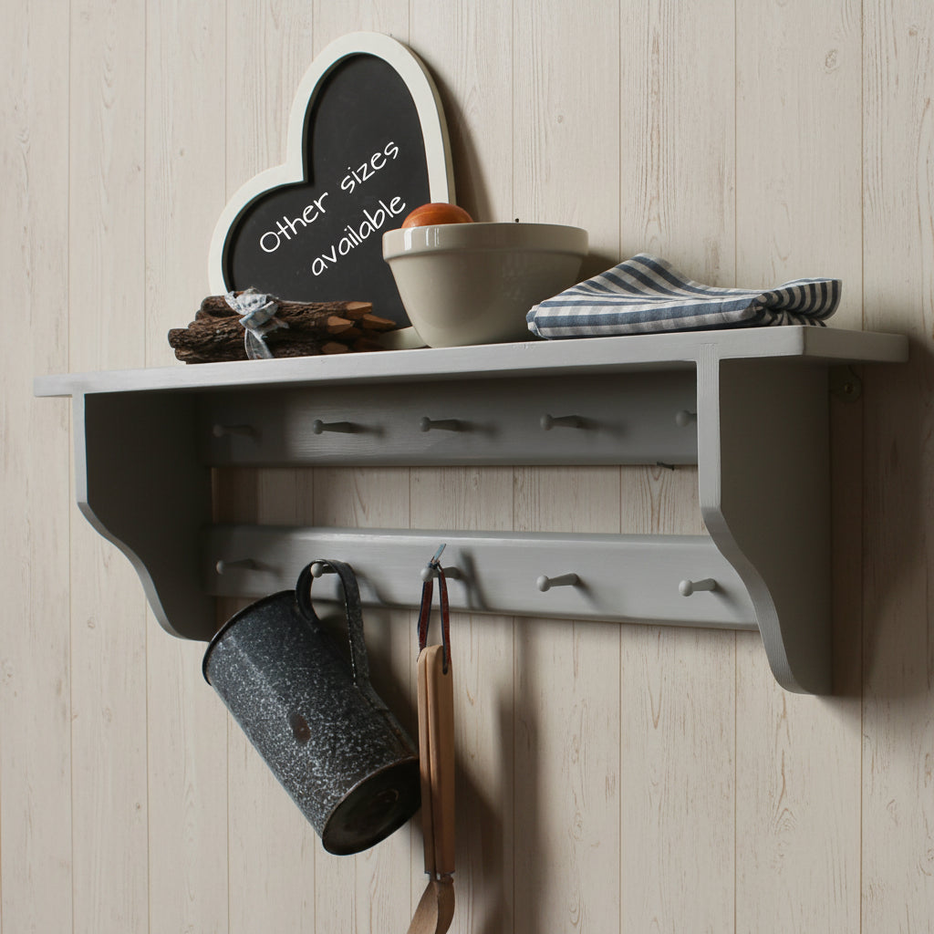 A gray wall-mounted shelf with hooks, shown against a beige wall with decorative items including a small chalkboard sign, bowls, a cloth napkin, and a hanging metal mug.
