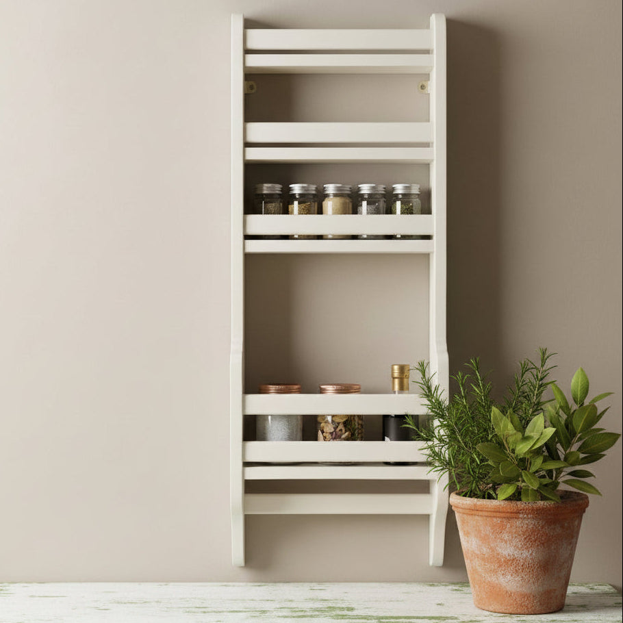 A tall, narrow white wall-mounted spice rack with multiple horizontal shelves, shown against a beige wall above a light wood surface. Several glass spice jars are placed on and beside the rack.
