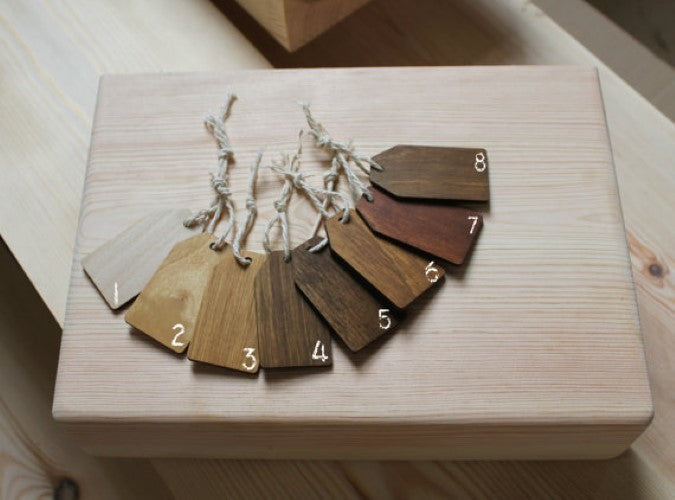 Eight numbered wood color and grain swatch tags arranged in a fan shape on a light wooden block, showing various natural wood tones from light beige to dark brown.
