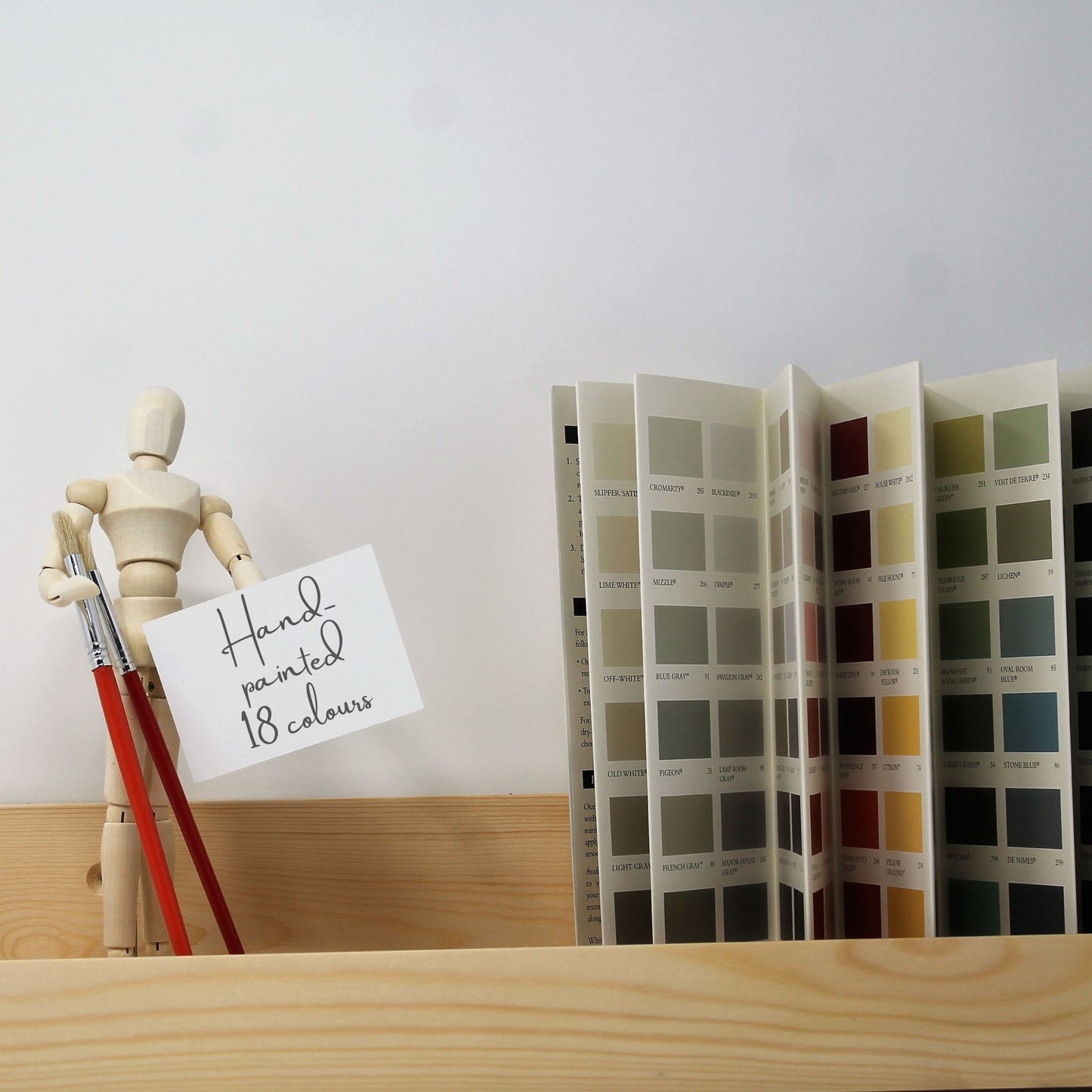 floating wooden ledge shelf holding a wooden mannequin and a Farrow and Ball paint colours chart