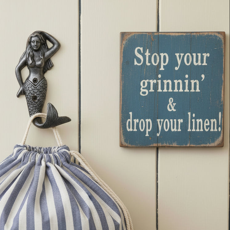 A cast iron mermaid wall hook with a textured, dark metallic finish, shown next to a wooden sign on a light wood background.
