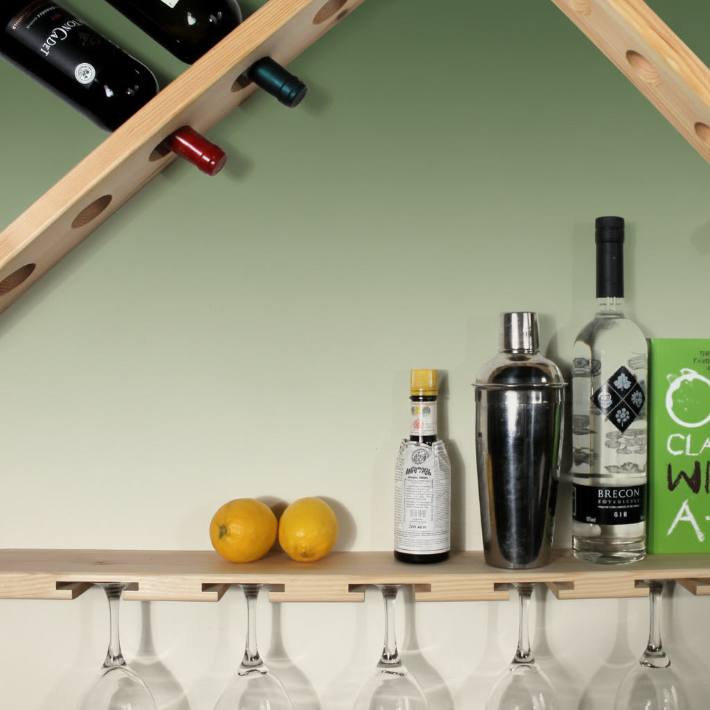 A wooden wall-mounted wine and glass holder with a triangular roof design, shown holding wine bottles, lemons, a cocktail shaker, and hanging wine glasses against a white wall.