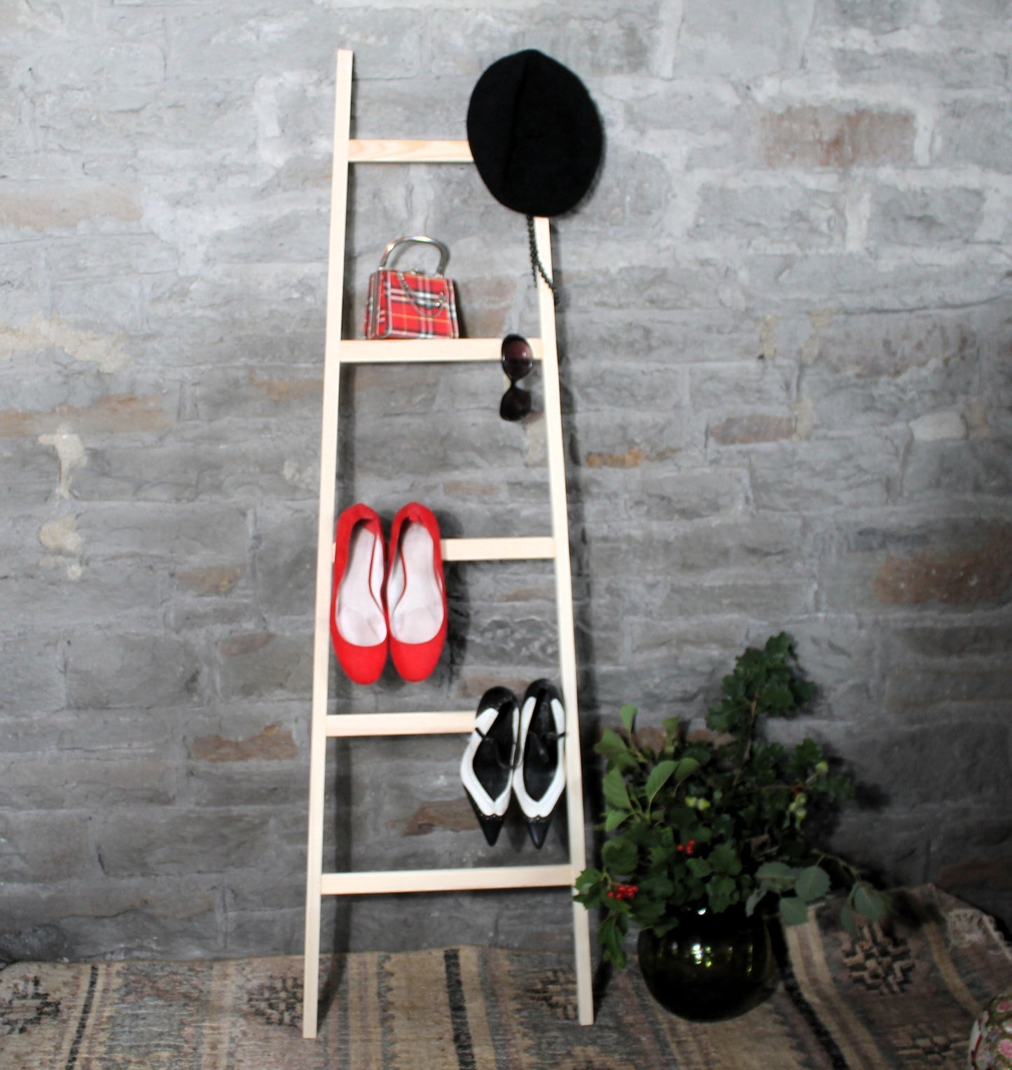Wooden beroom valet ladder with shoes and a hat against a stone wall