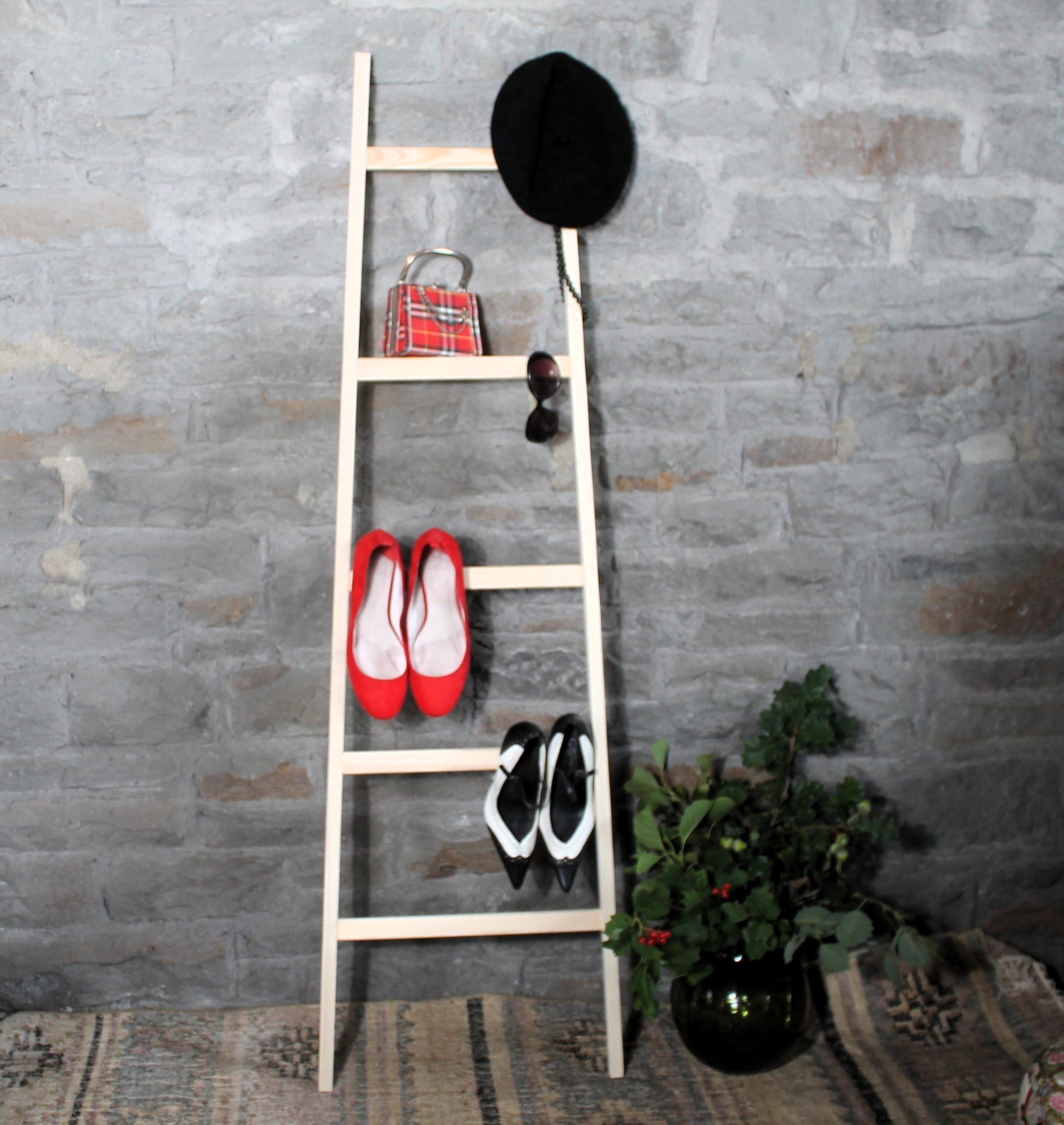 Wooden beroom valet ladder with shoes and a hat against a stone wall