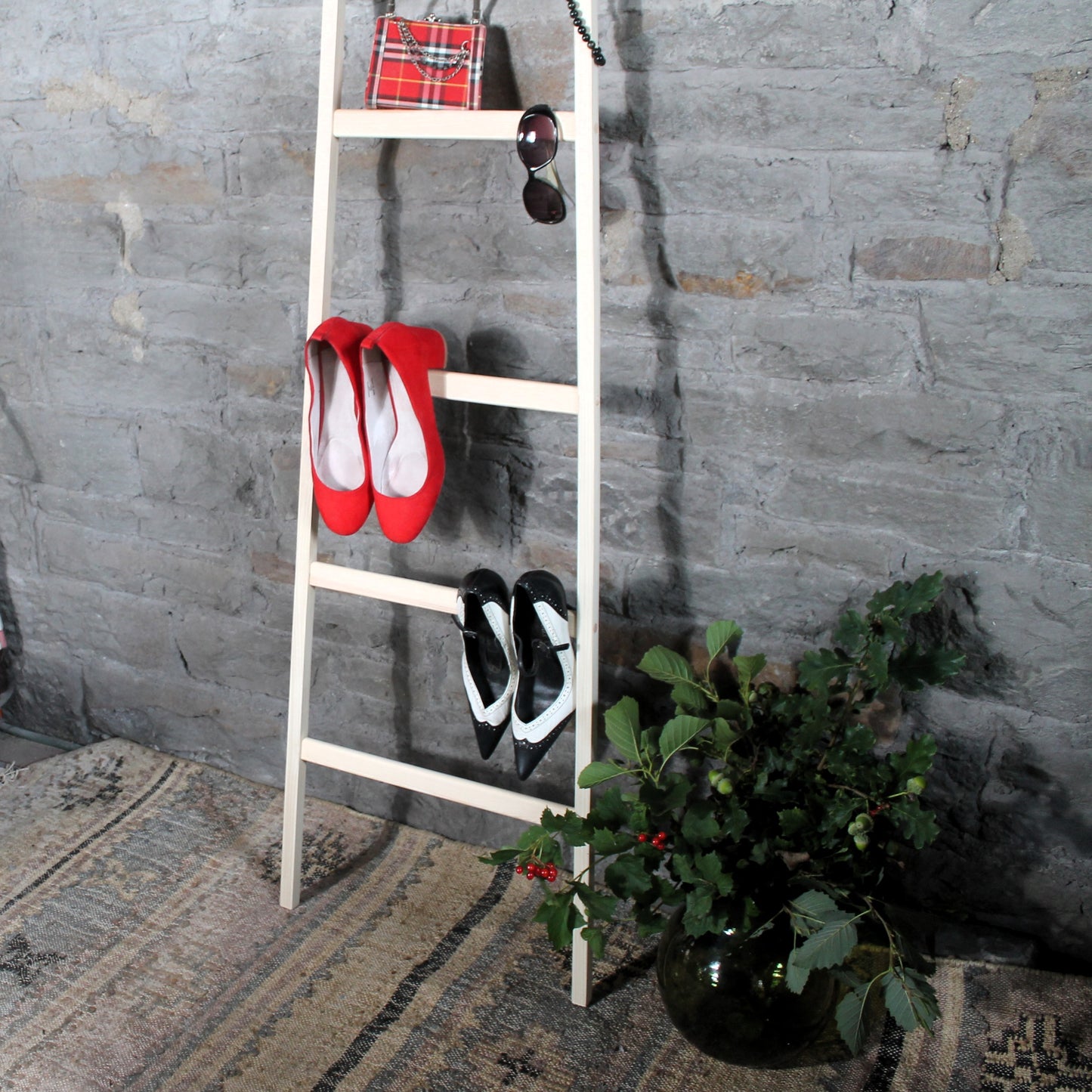 Rustic wooden valet ladder with red shoes, black shoes, and a plant against a stone wall.