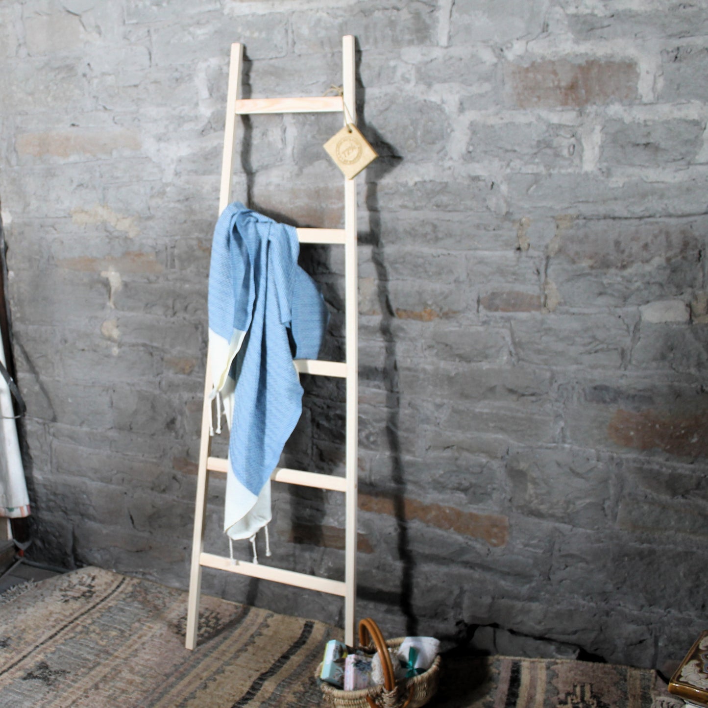 Wooden towel rack  ladder with a blue towel against a stone wall