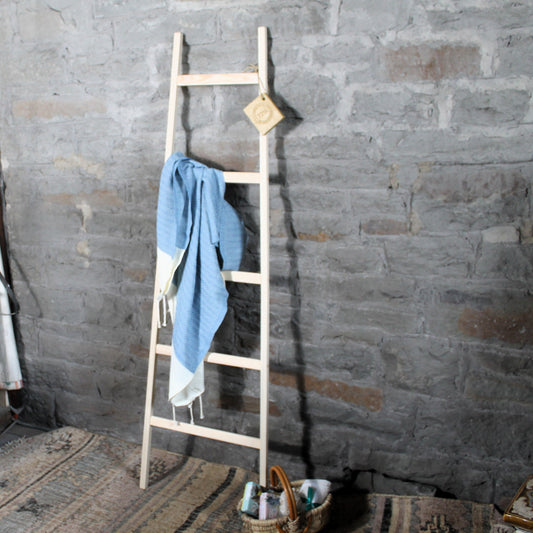 Wooden towel rack  ladder with a blue towel against a stone wall