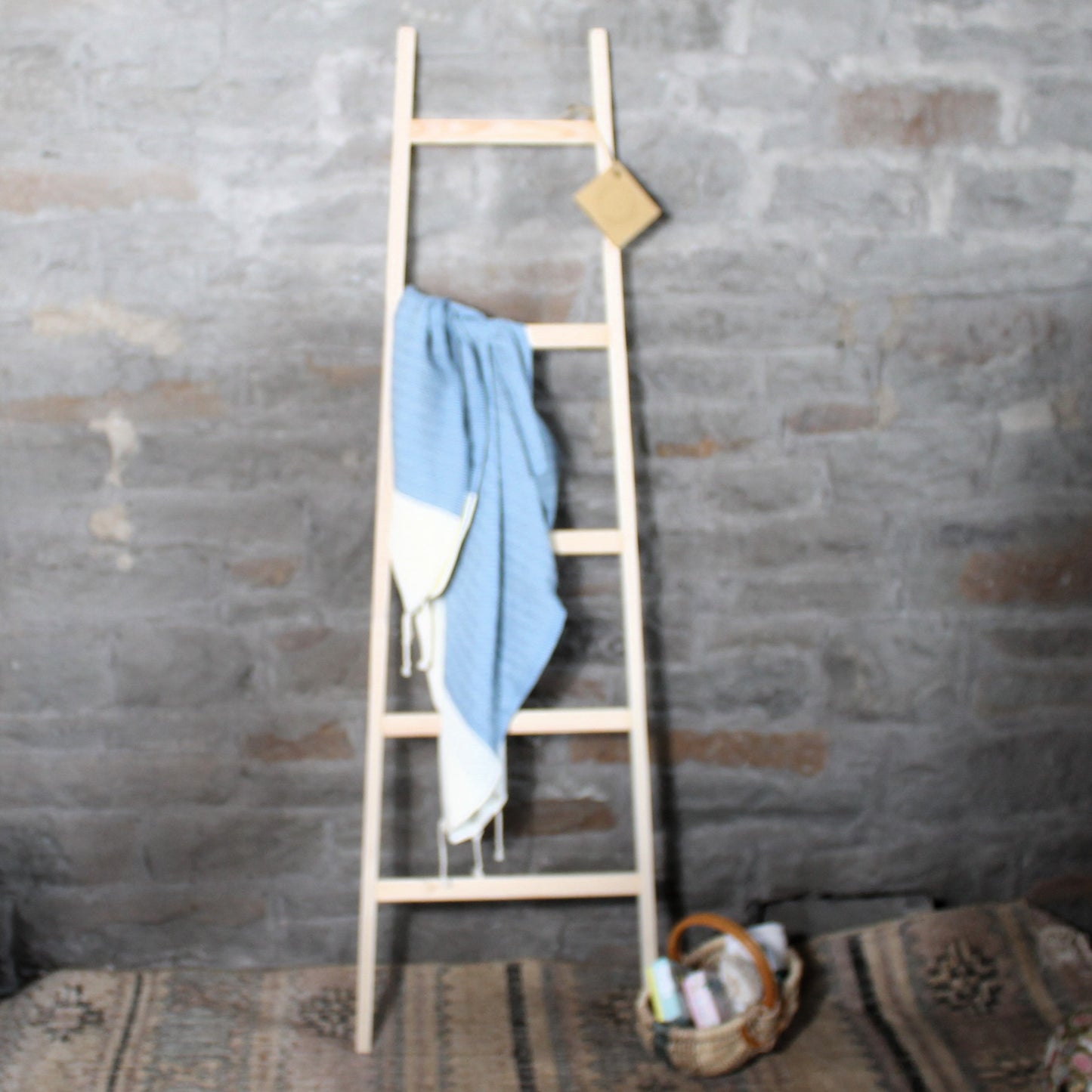 Wooden bathroom towel ladder with a blue towel against a stone wall