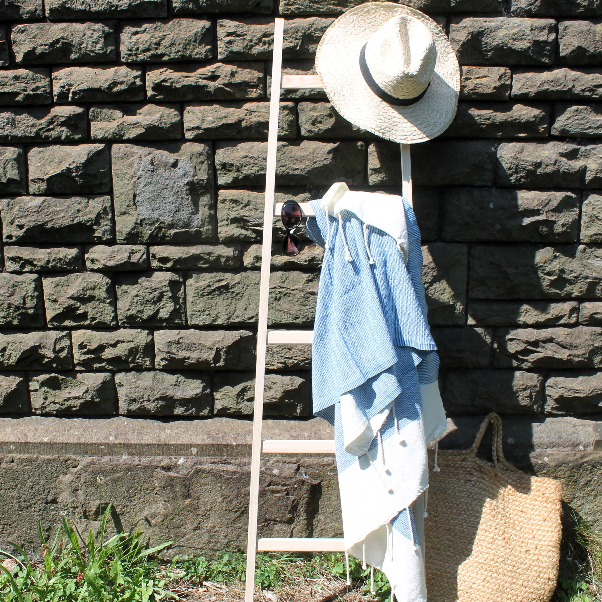 Minimalist wooden clothess ladder with clothing and a hat against a stone wall