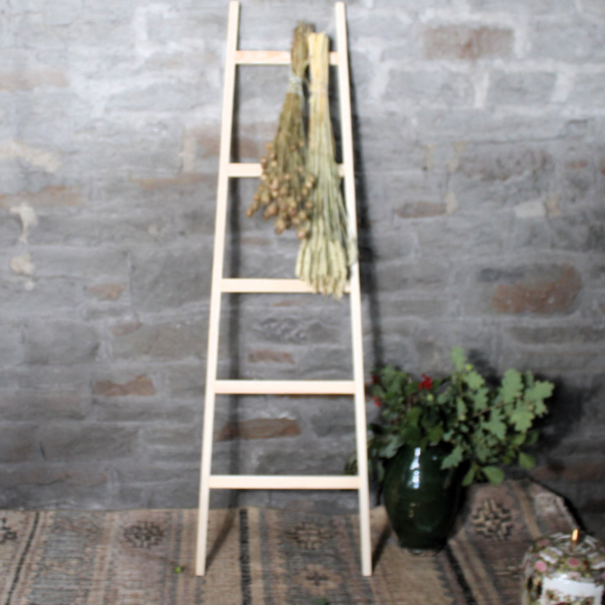 Wooden ladder with for herbs and flowers drying with plants against a stone wall.