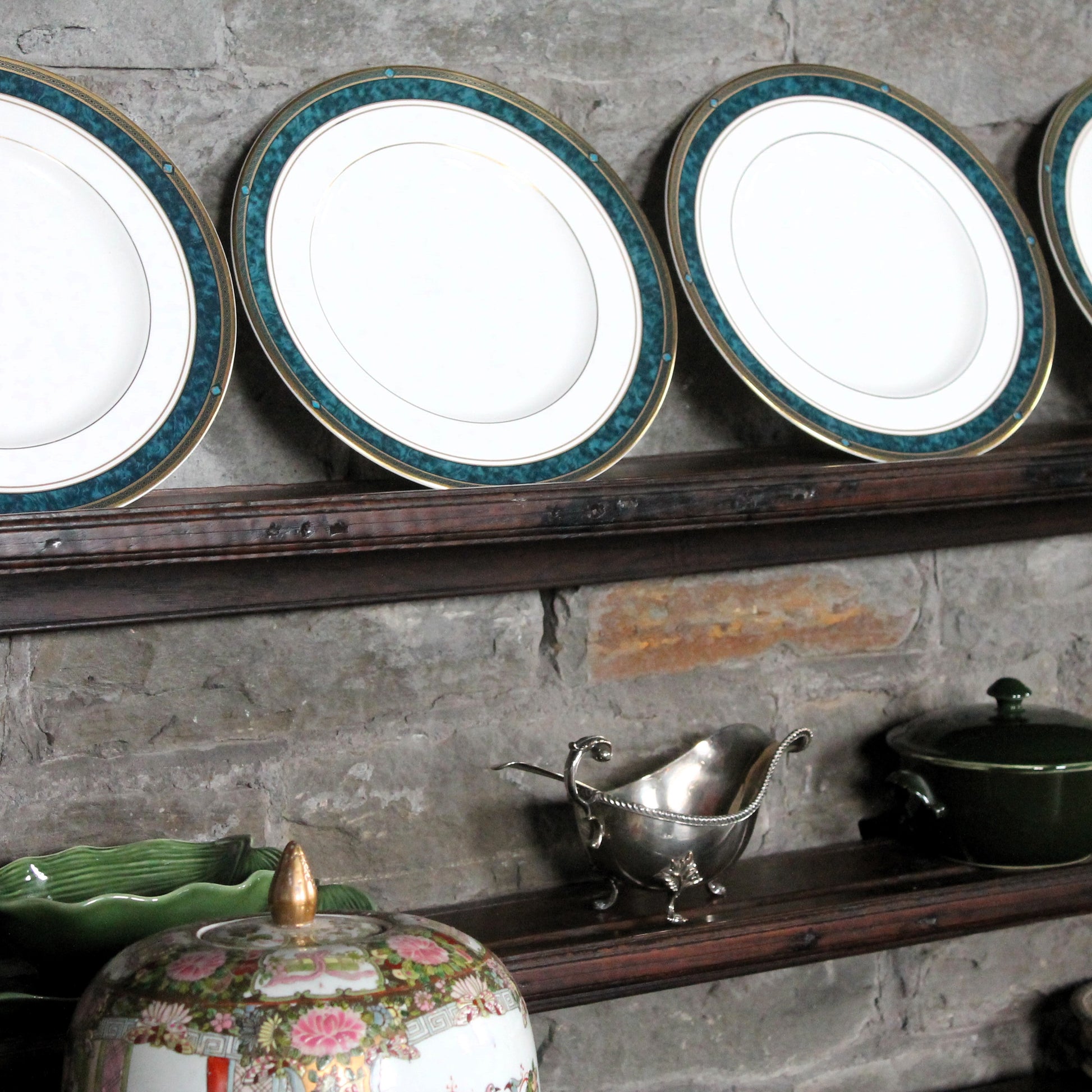 Set of Royal Doulton dinner plates with green and gold trim on a rustic wooden shelf against a stone wall.