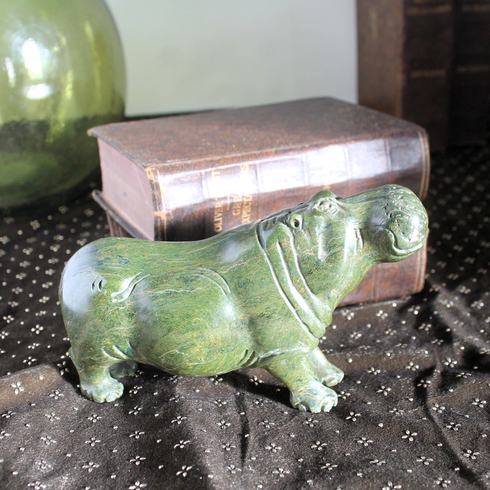 Carved stone hippo on a velvet cloth with books in the background