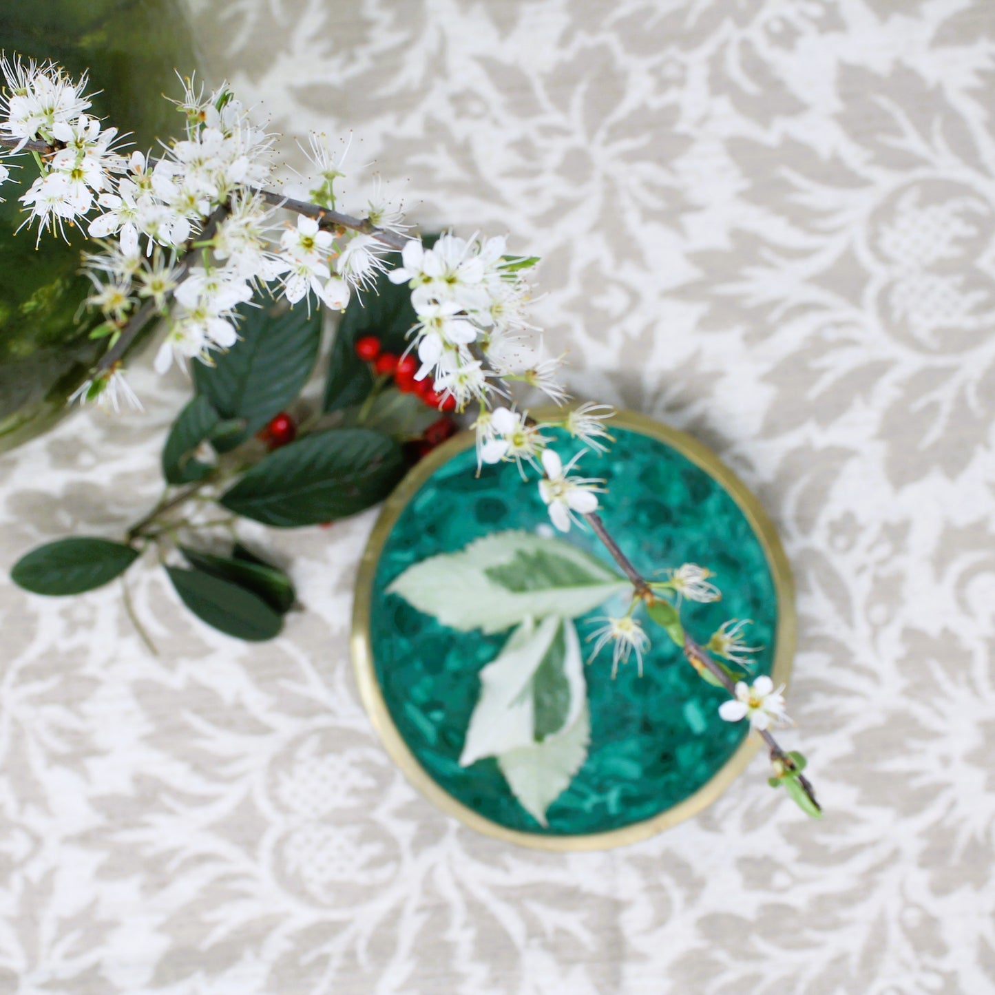 Artisan malachite bowl with brass edge shown on a damask cloth with leaves and flowers