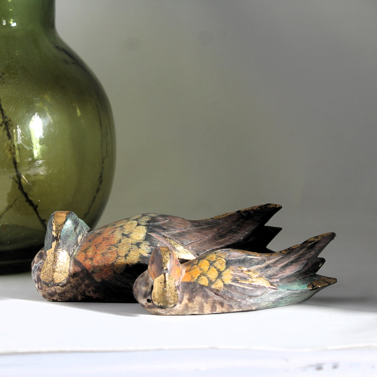 Decorative wooden mother duck and duckling figurine with a green ceramic vase in the background