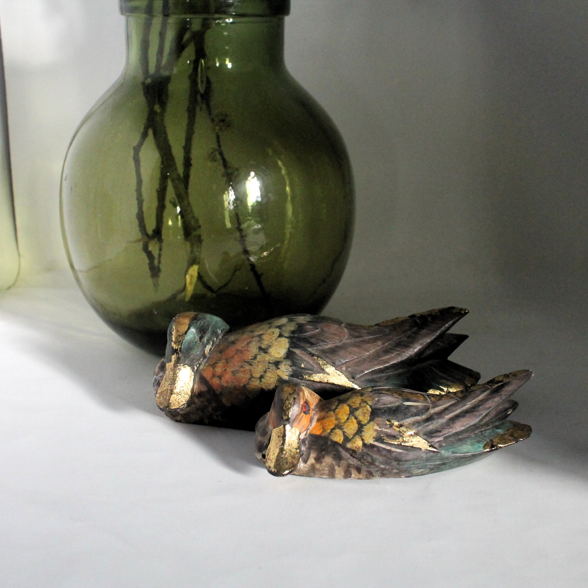 Pair of decorative duck sculpture with a green glass bottle on a light background