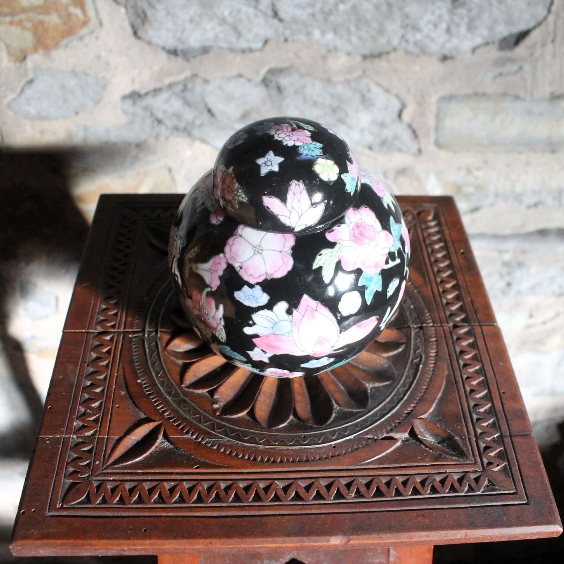 small famille noire Chinese ginger jar on a wooden pedestal on a stone background