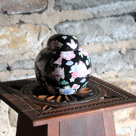 Chinese porcelain black ginger jar with flowers on a wooden pedestal against a stone wall