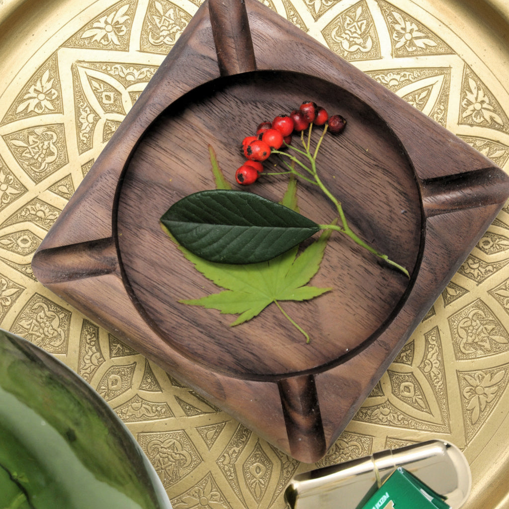 A square dark brown wooden serving board with a circular inset, styled with green leaves and red berries on a white surface.