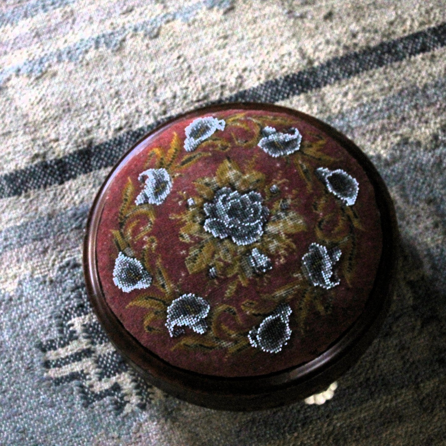 Round footstool with embroidered fabric covering  in a floral beaded pattern on a textured surface