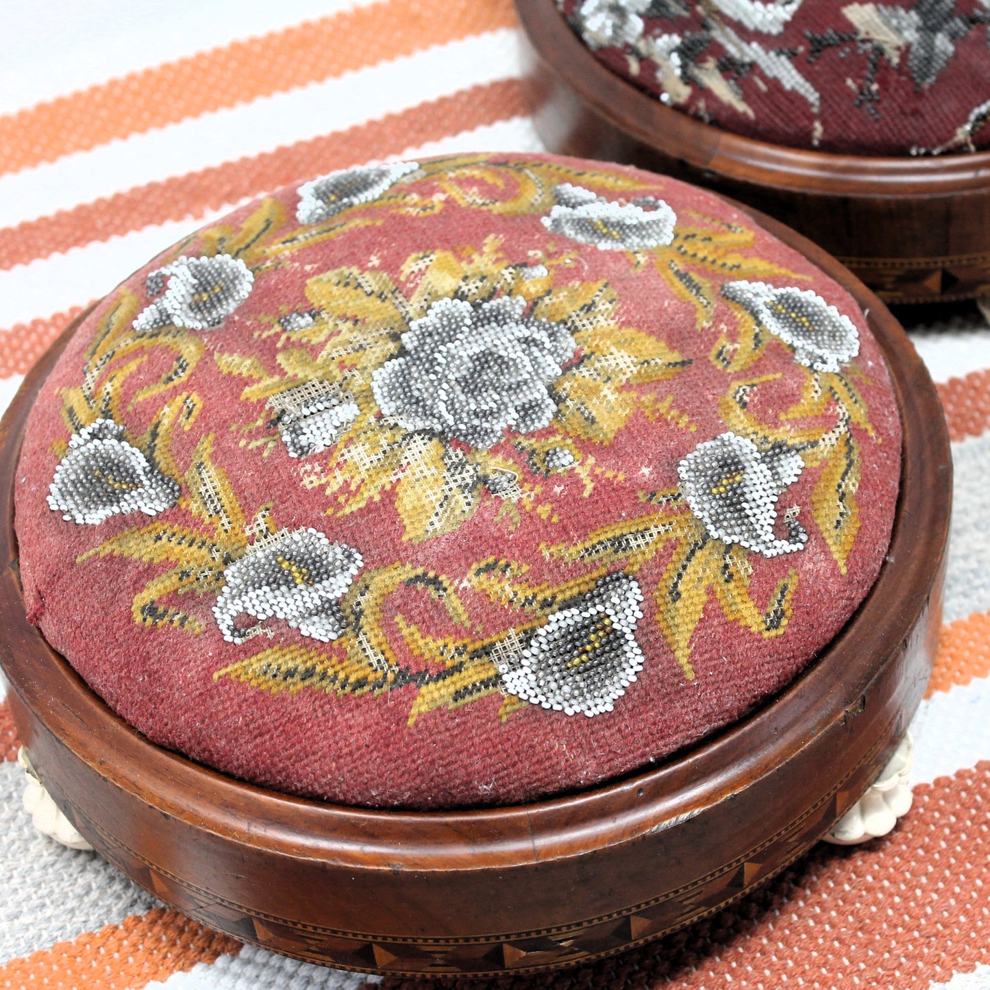 Round fabric antique footstool with floral pattern in a wooden frame on a striped fabric background