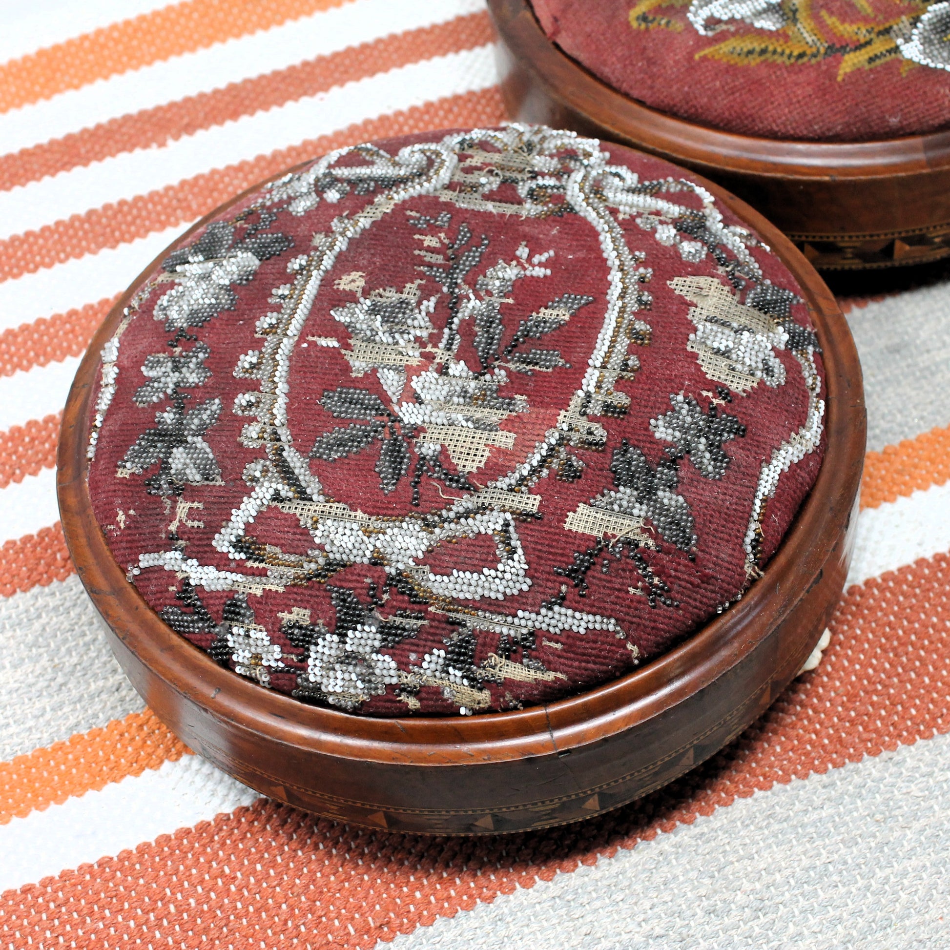 Decorative wooden footstool with needlepoint and beading floral pattern on a striped fabric background