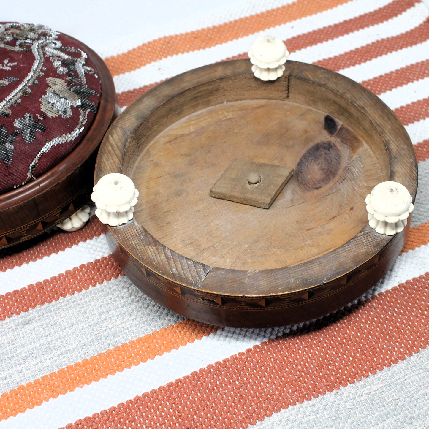 Wooden underside of Victorian footstool with ceramic feet on a striped fabric background