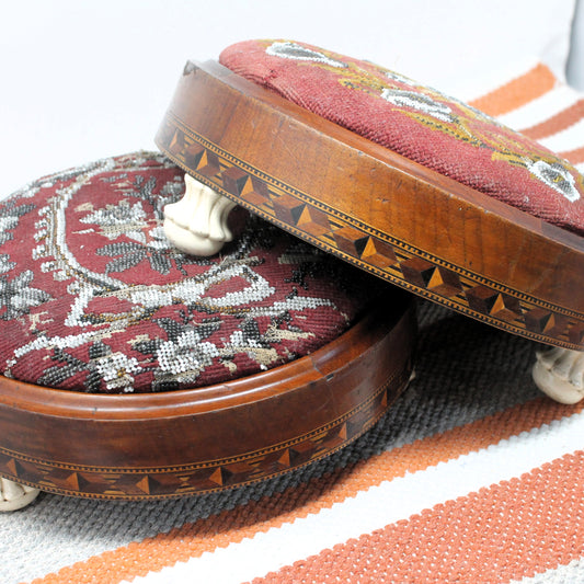 Two wooden footstools with patterned fabric seats on a striped rug.
