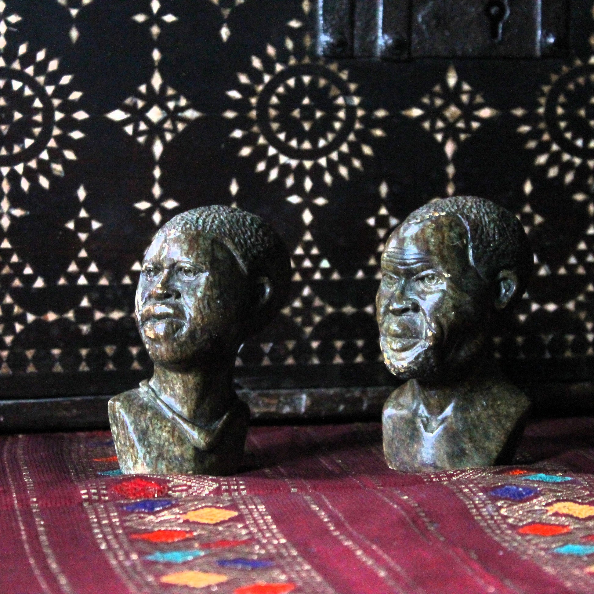 Two Kenyan kisii stone carvings  busts on a textured surface with a patterned background