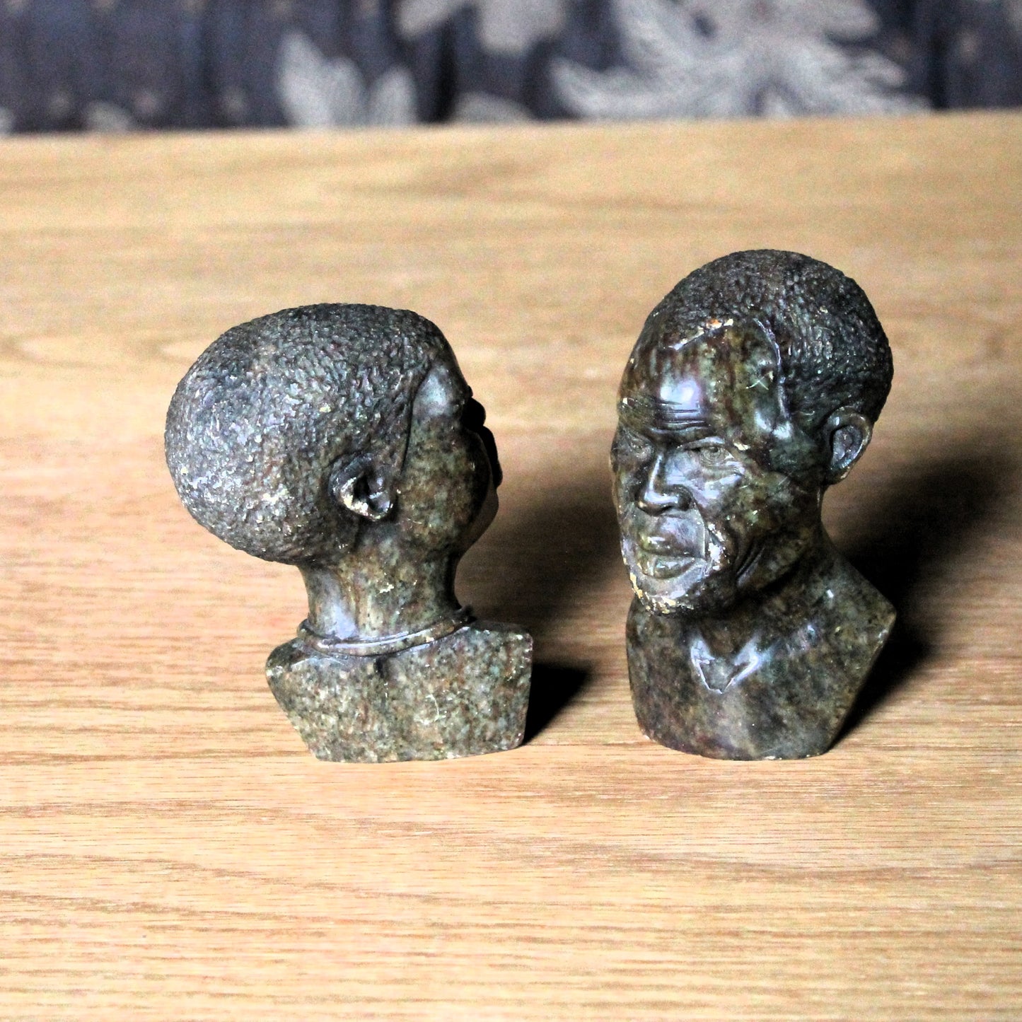 Two stone sculptures of human heads on a wooden surface