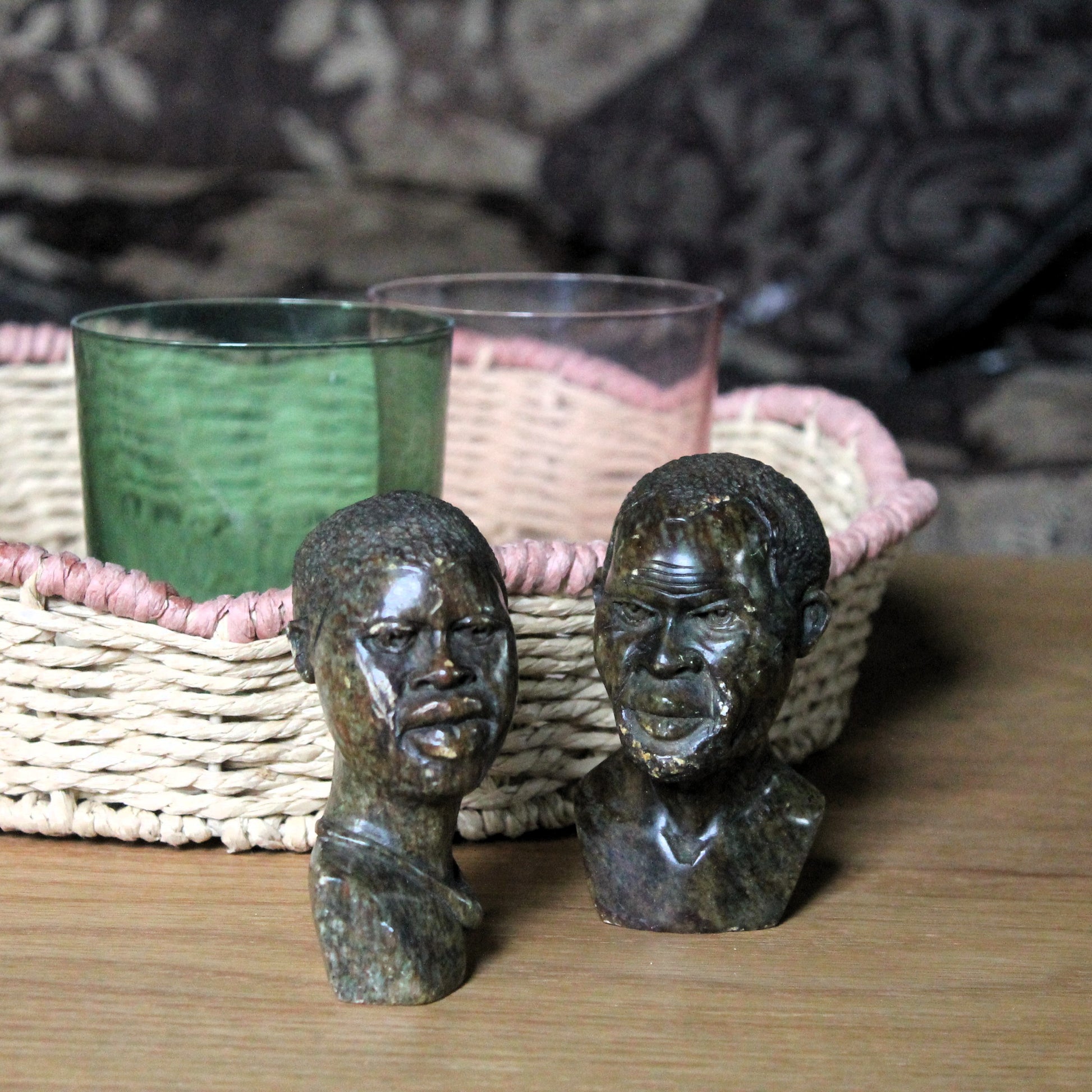 Two stone sculptures of faces on a wooden surface with wicker baskets in the background.