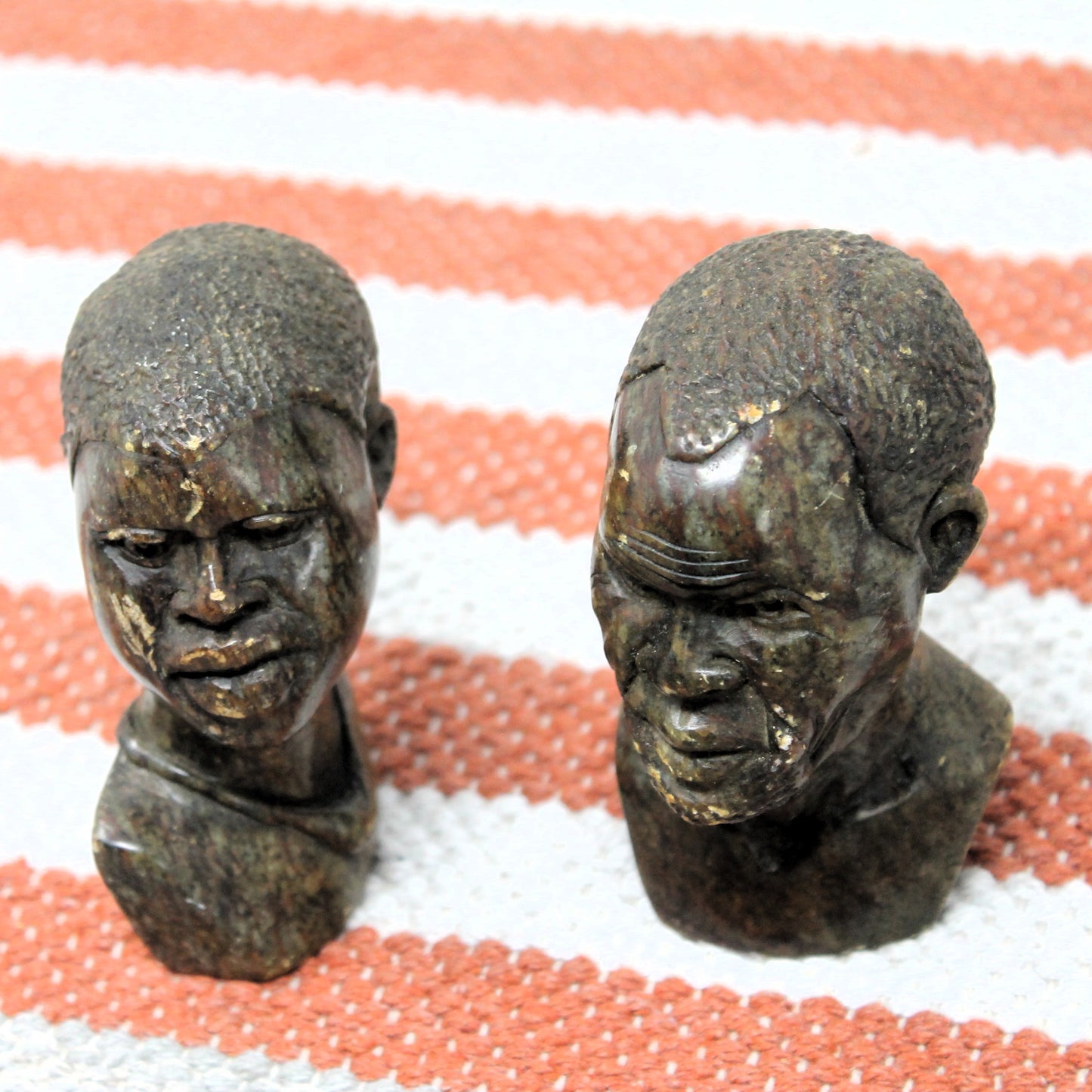 Two Kisii sculptures of human heads on a striped fabric background