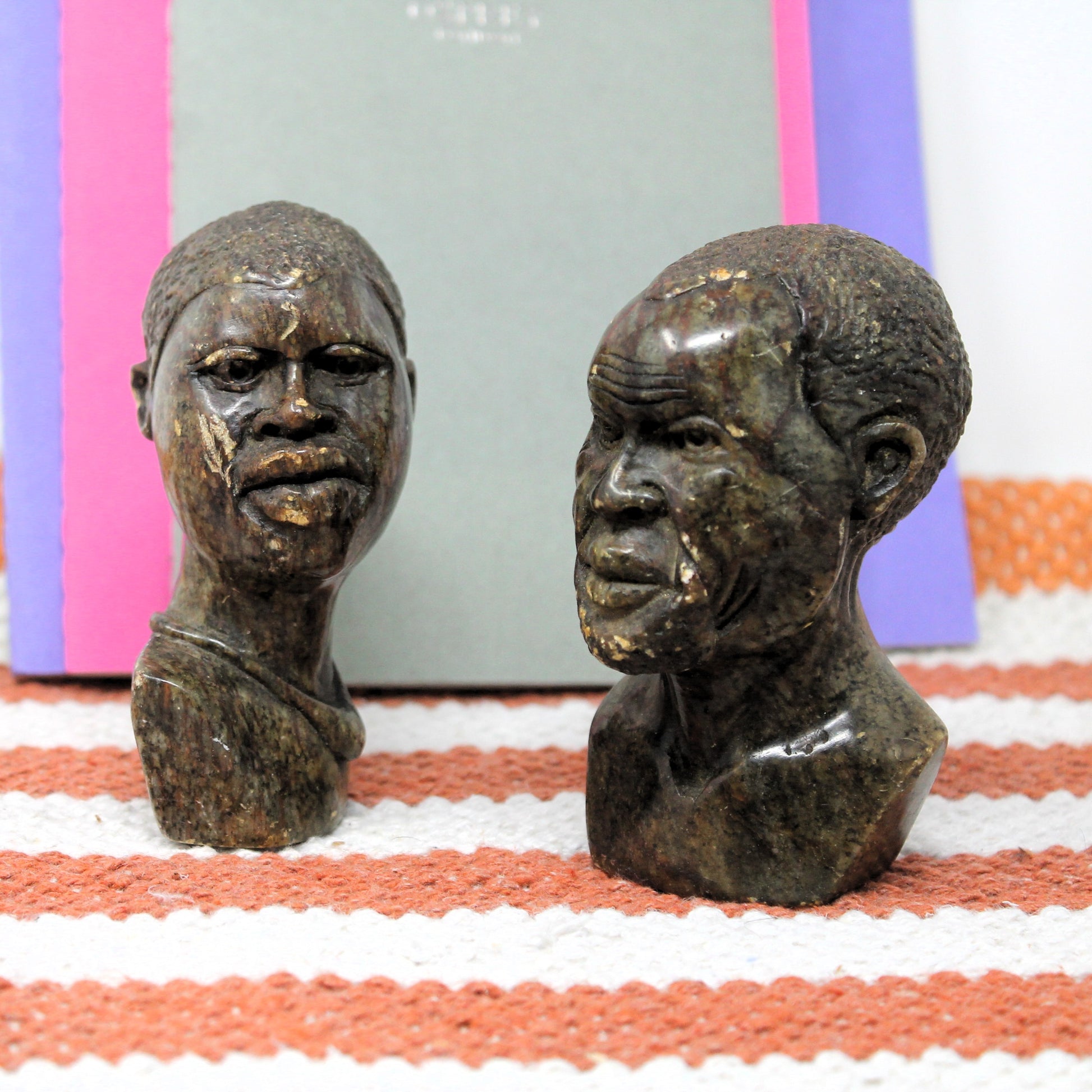 Two Kenyan sculptures of human heads on a striped fabric background