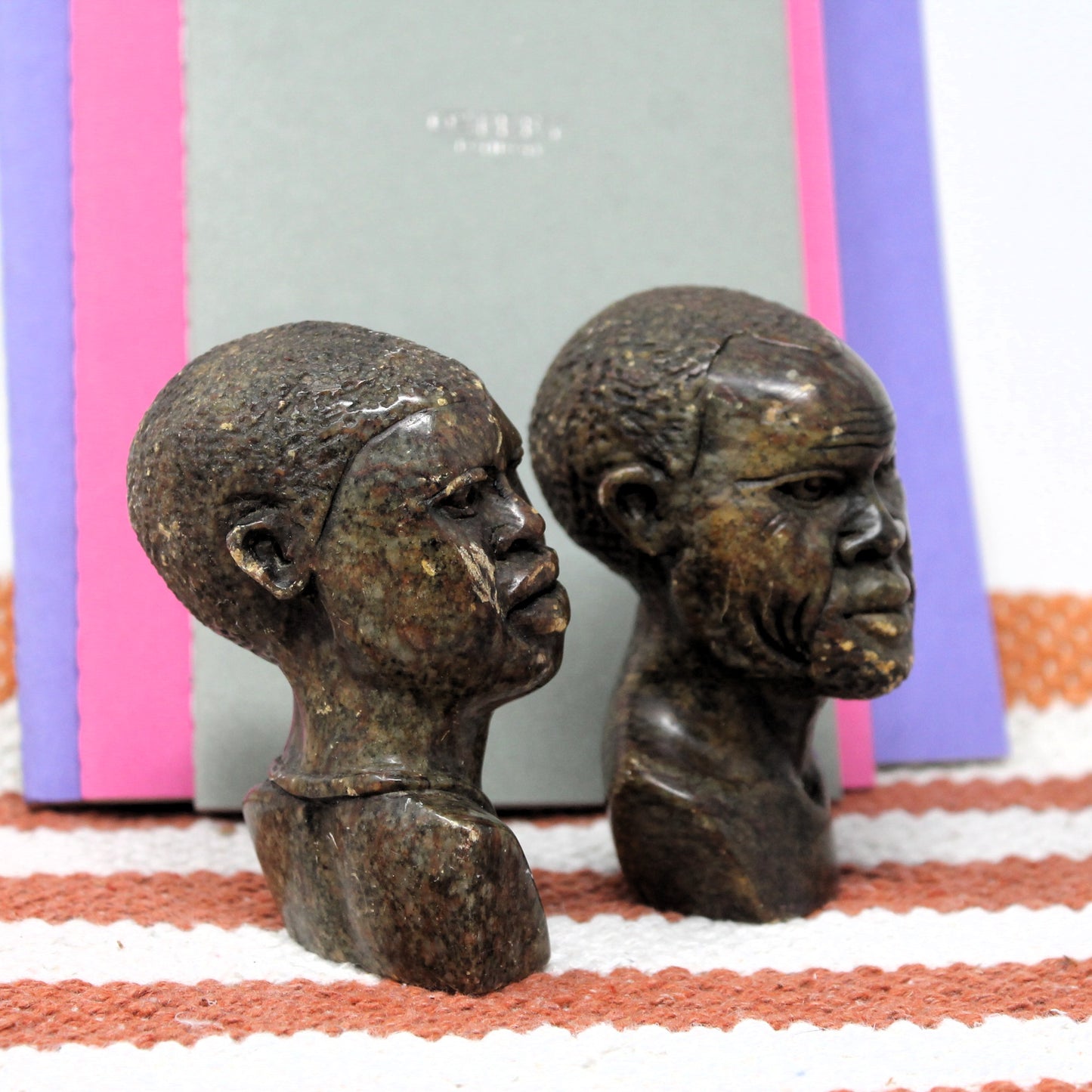 Two stone sculptures of African heads on a striped background
