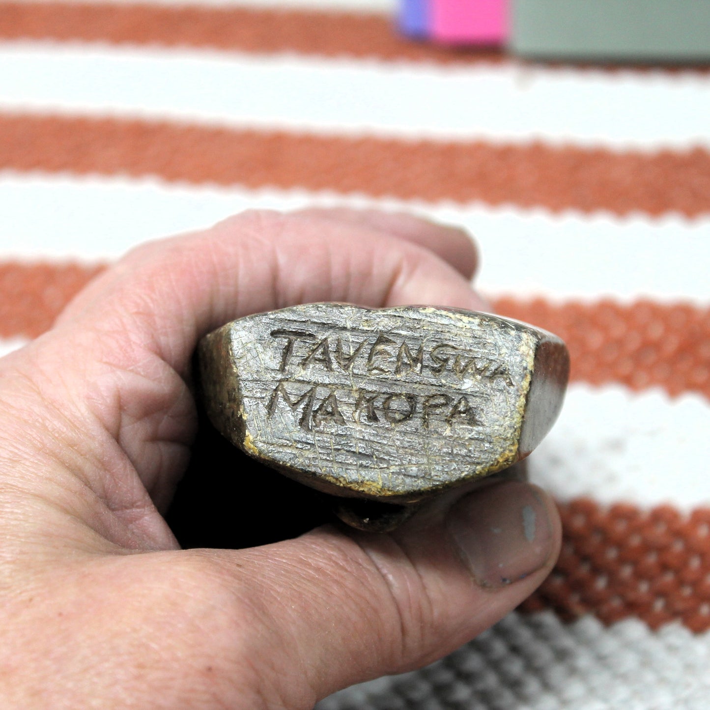 Hand holding a stone object with engraved text against a striped fabric background