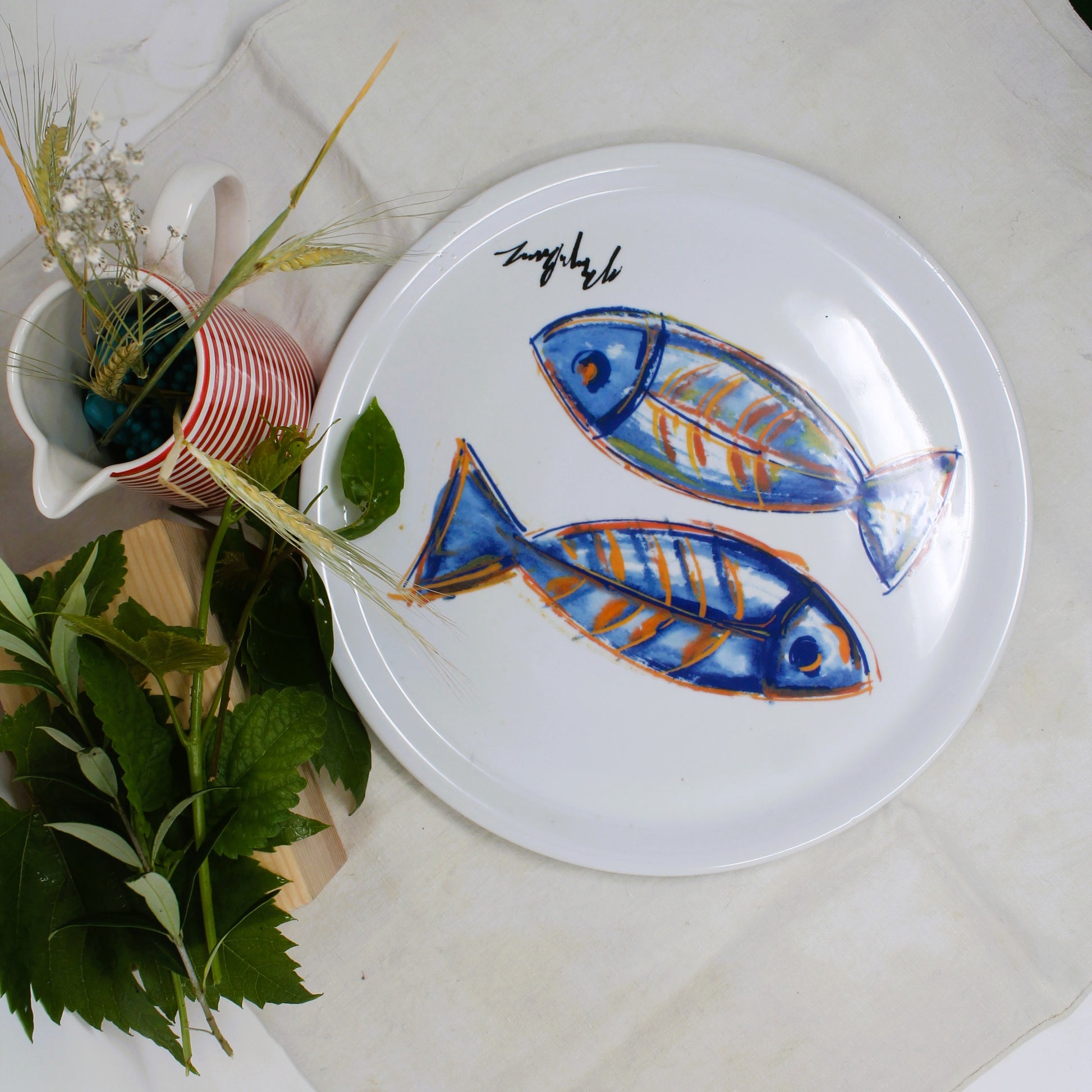 Bofrost decorative  plate with fish design on a light surface with plants and a pitcher.
