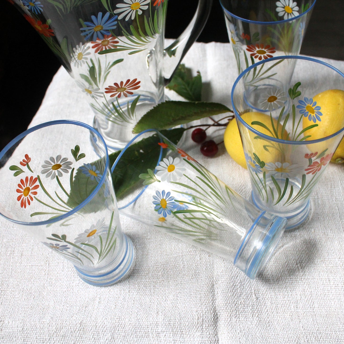 Set of floral-patterned glasses on a white tablecloth with lemons and berries.