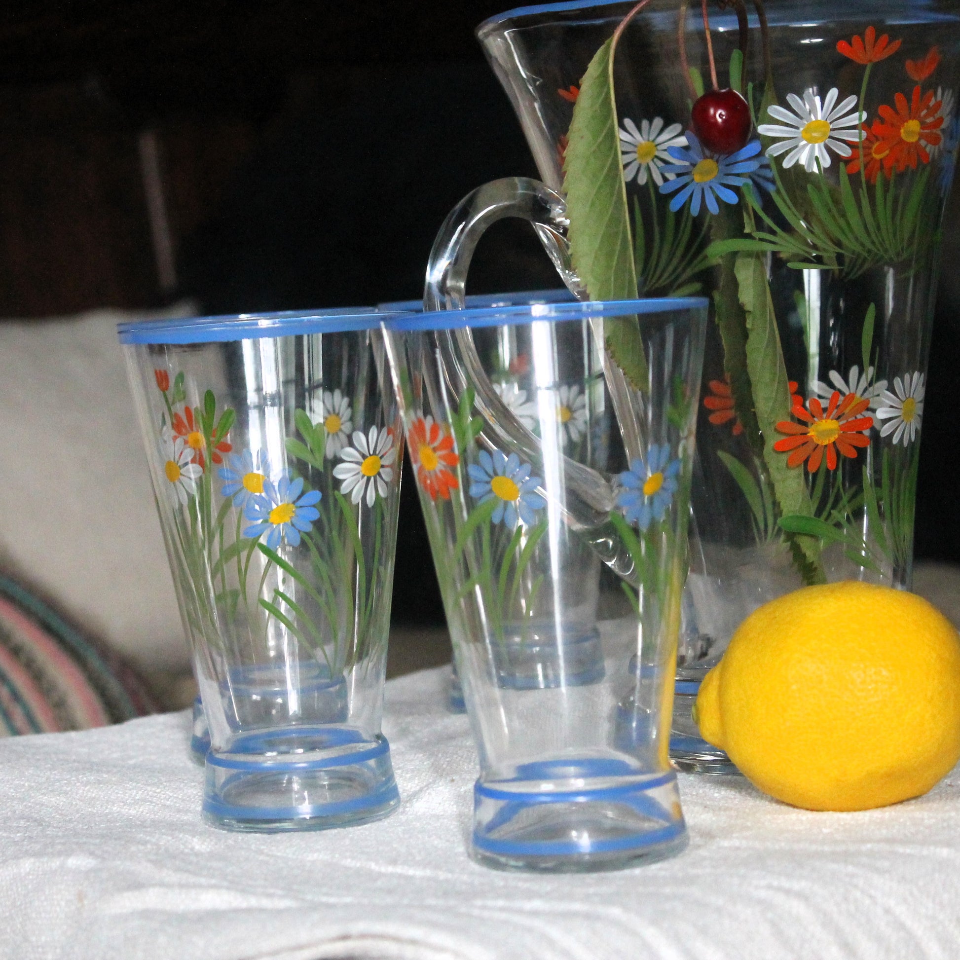 Two floral-patterned glasses with a pitcher and lemon on a table.