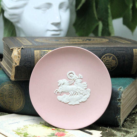 A rounddusky pink Wedgwood  trinket dish with a white embossed relief of a rider on a horse, styled on top of vintage books with a white decorative bust in the background