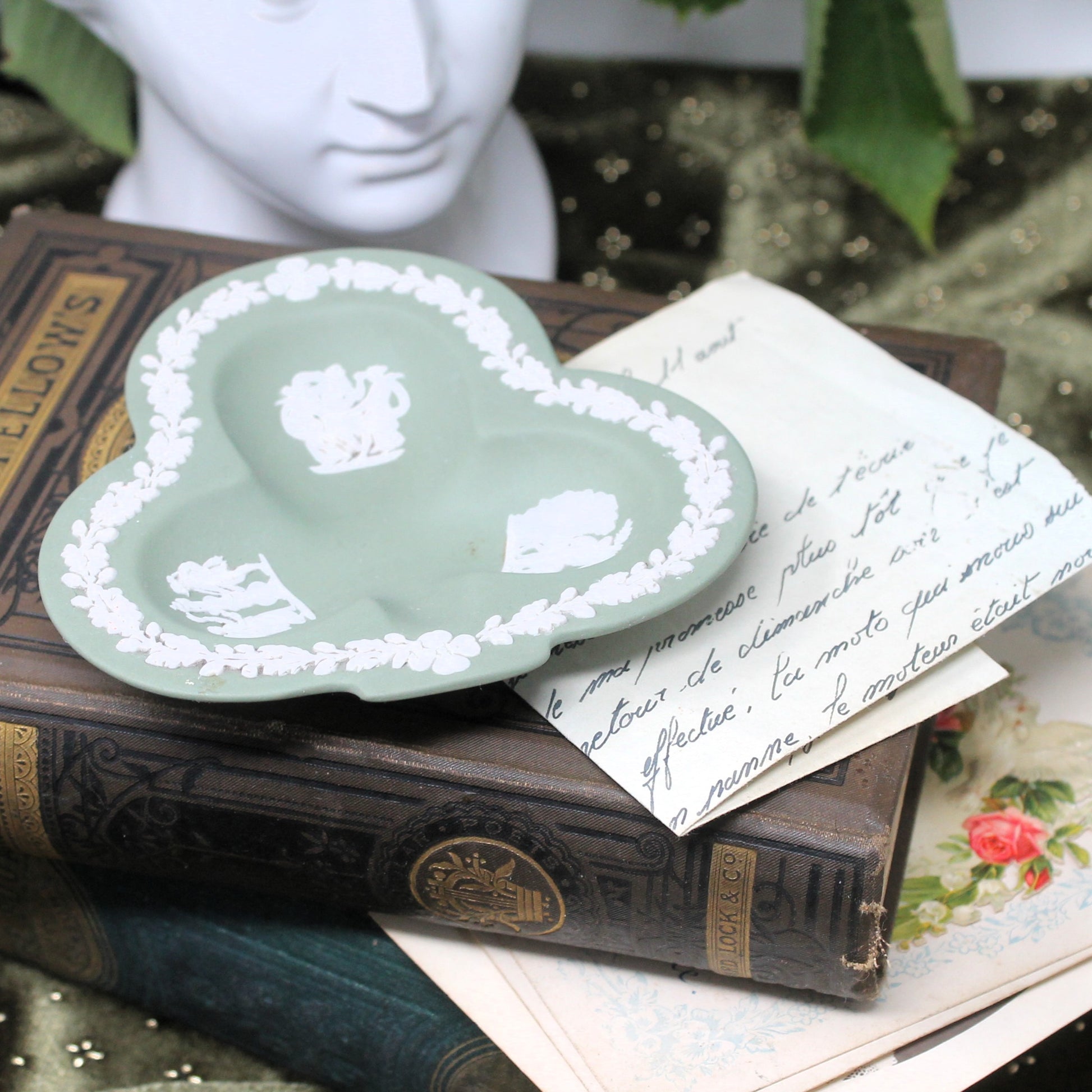 Trefoil-shaped green Wedgewood  dish with white floral patterns on top of vintage books