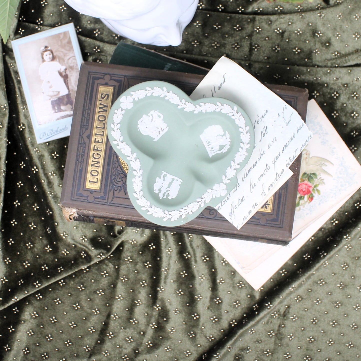 Trefoil-shaped Wedgewood dish on top of books with vintage photo and card on a patterned fabric background