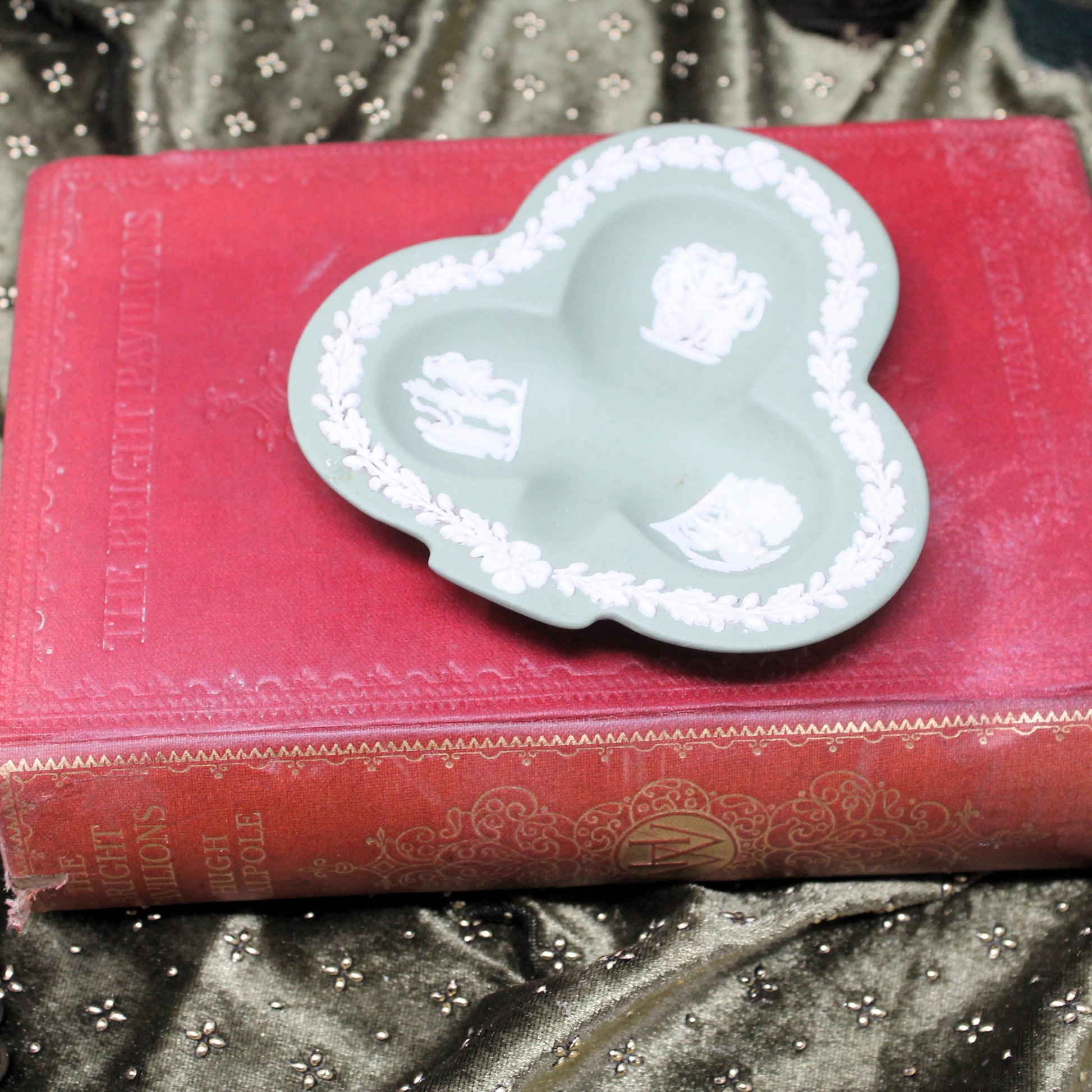 Decorative green trefoil-shaped trinket dish on a red book with gold text