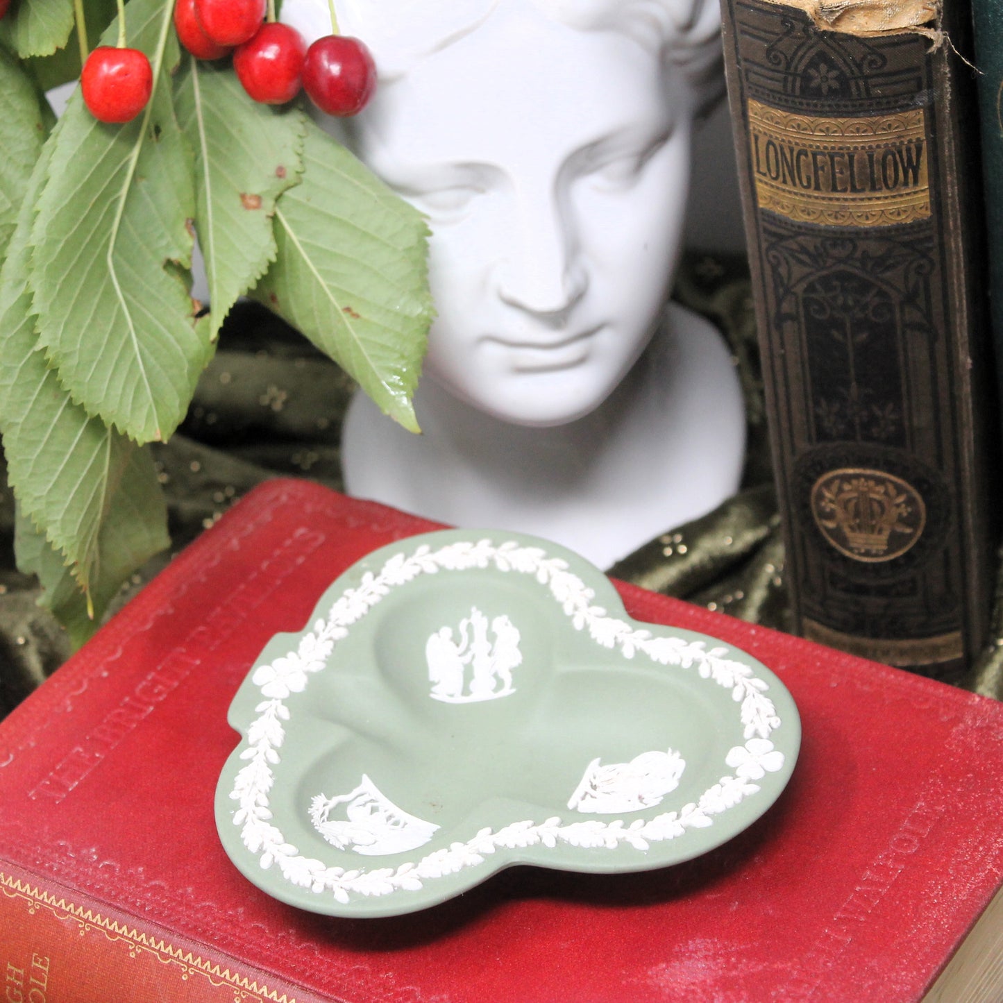 Trefoil-shaped Wedgewood dish on a red surface with a bust and book in the background