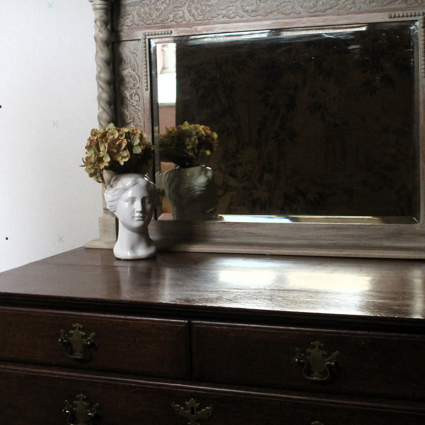 Decorative mirror with a vase of flowers and a sculpture on a wooden surface.