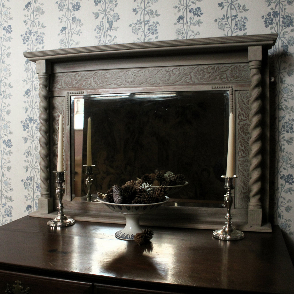 Carved wooden mirror frame with candles and decorative items on a wooden surface.