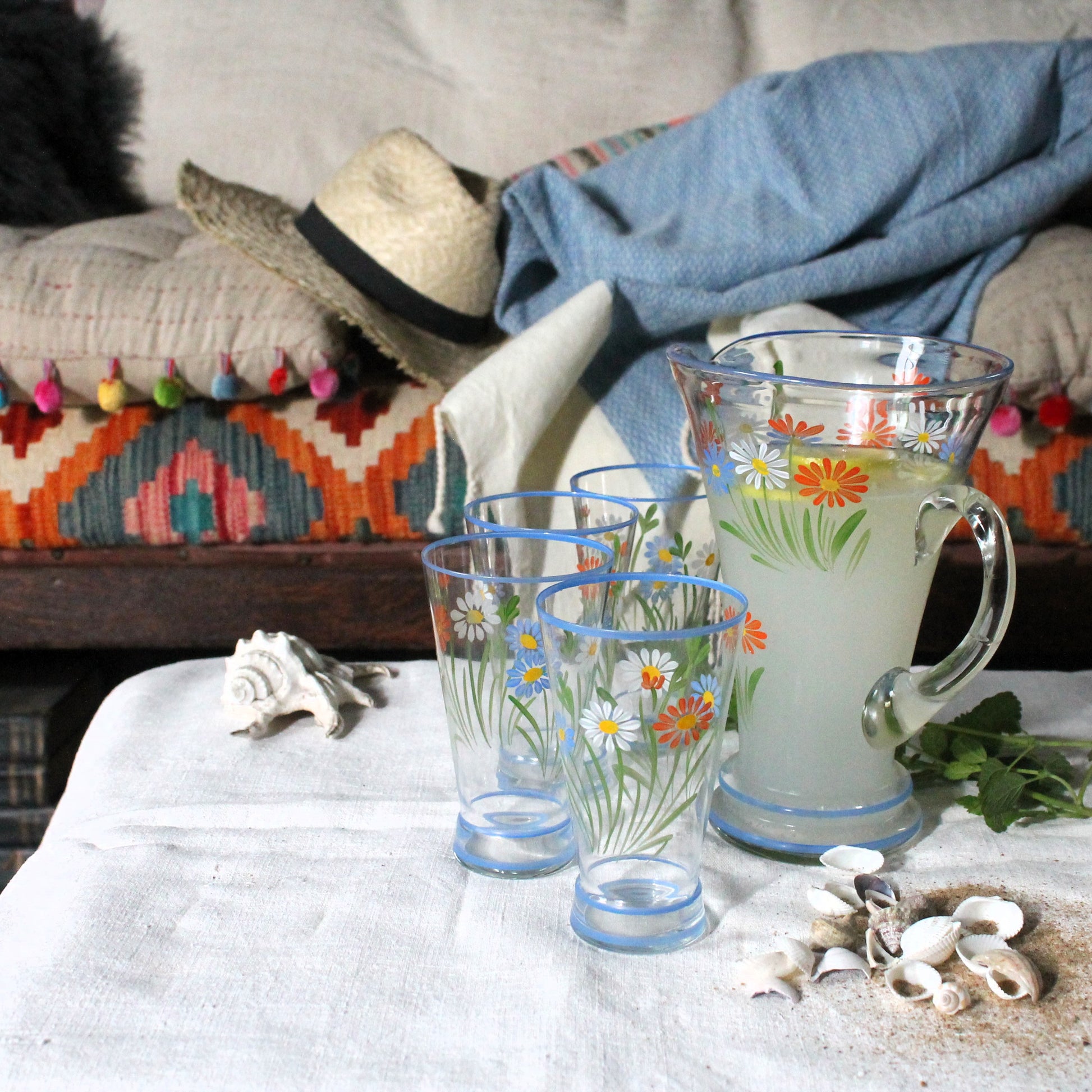 Set of floral glassware on a table with decorative pillows and a hat in the background