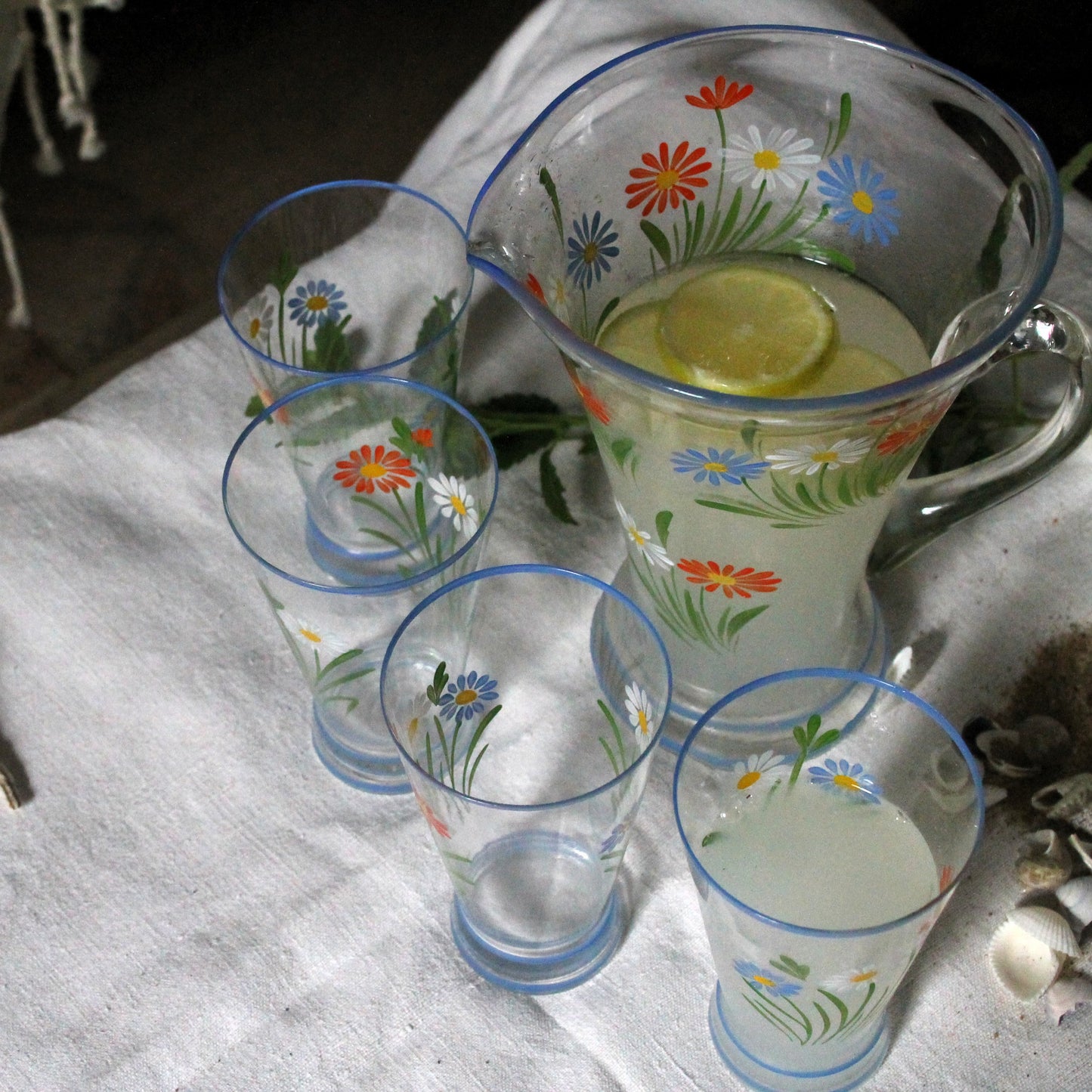 Set of floral-patterned glasses and a pitcher with lemon slices on a white cloth.