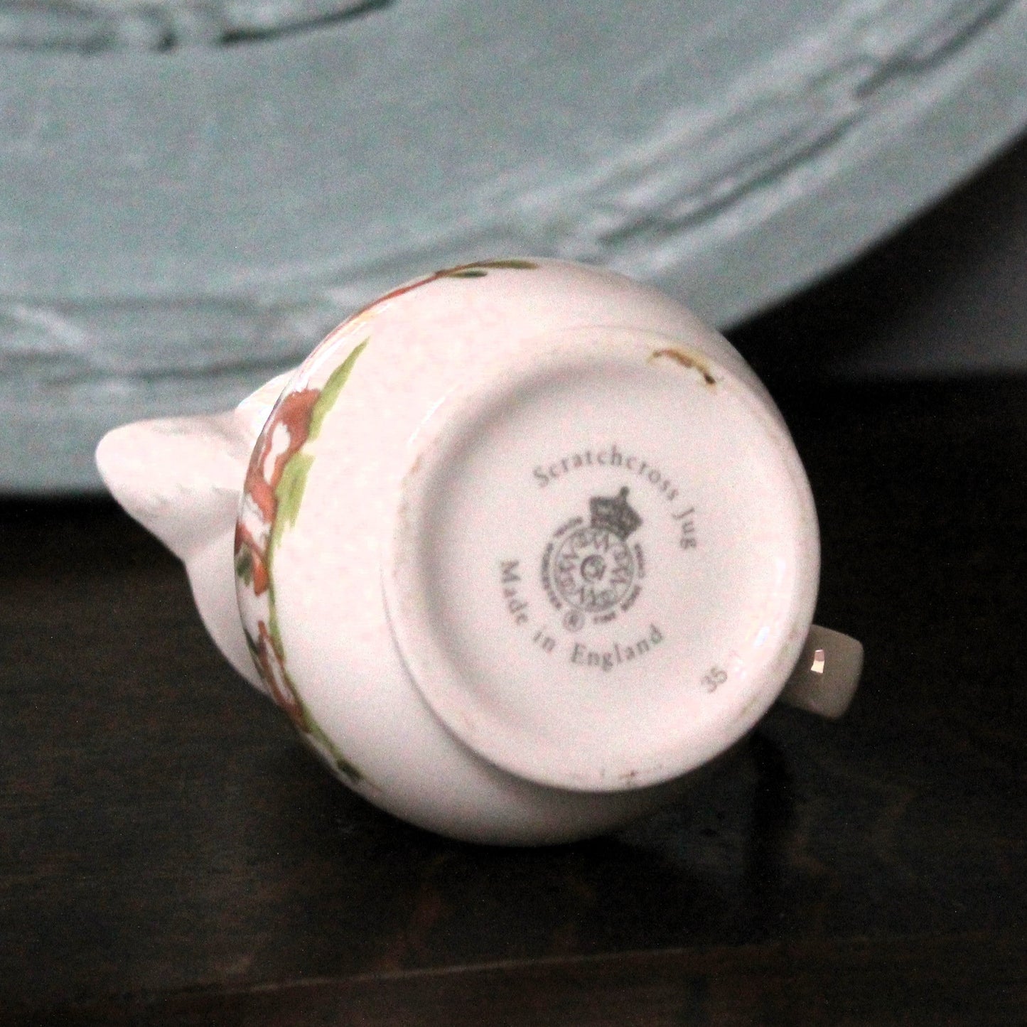 A vintage Royal Worcester porcelain jug shown upside down on a dark wooden surface, displaying its printed 'Scratchdown No. 36 Made in England' mark. 